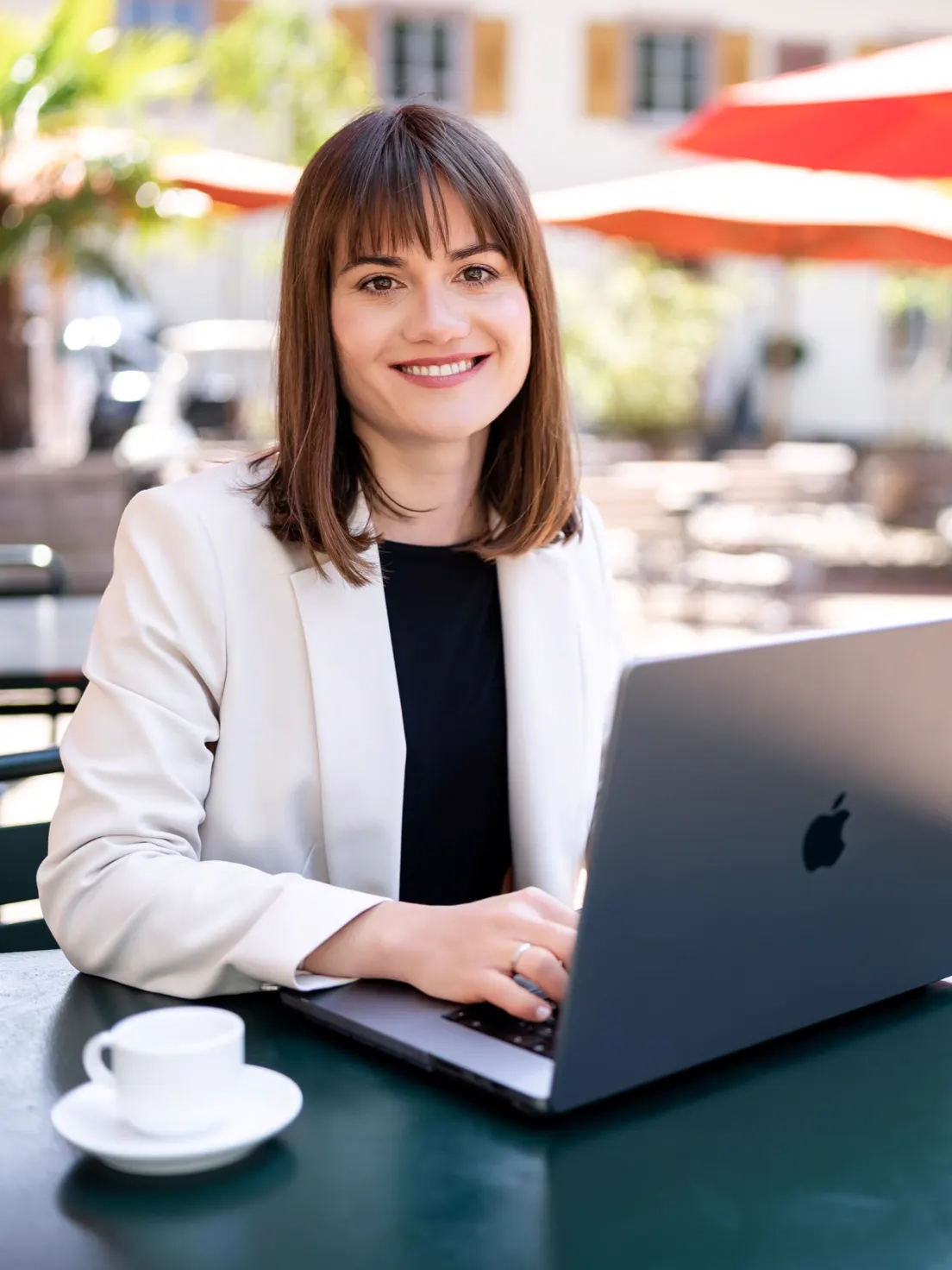 Melanie, Beraterin für Hochzeitslocations, arbeitet lächelnd an einem Laptop vor einer Hochzeitslocation